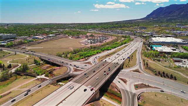 Overhead drone view of busy highway interchange with moving traffic and Rocky Mountains backdrop