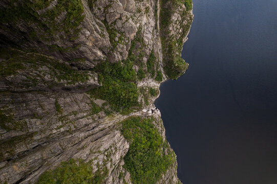 Aerial view of the sheer granite cliffs of Pulpit Rock dropping into the dark waters of Lysefjord, with lush green vegetation in Strand, Rogaland, Norway.