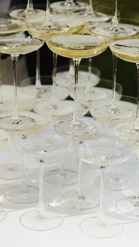 Vertical video. Champagne glass tower in close-up with the wedding couple softly blurred behind.