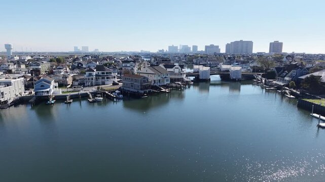 Drone pan view of a smooth bay with a small bridge being repaired in a shore town with tall buildings in the background