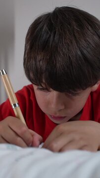 Young boy writing in notebook while resting on bed, highlighting relaxed learning, creativity and childhood education