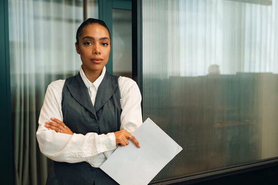 Portrait of confident businesswoman holding document while posing with arms crossed at office