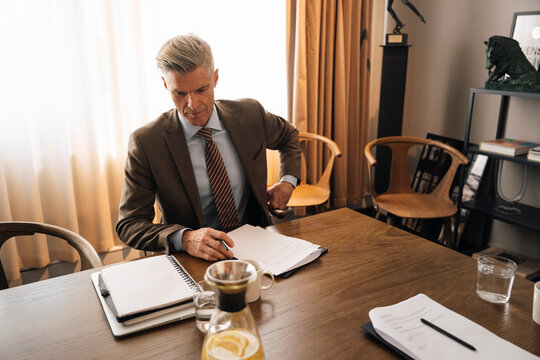 Senior businessman with documents sitting at wooden table in meeting room at office
