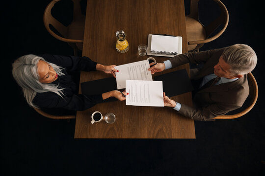 Directly above shot of senior business professionals exchanging documents while sitting at wooden table