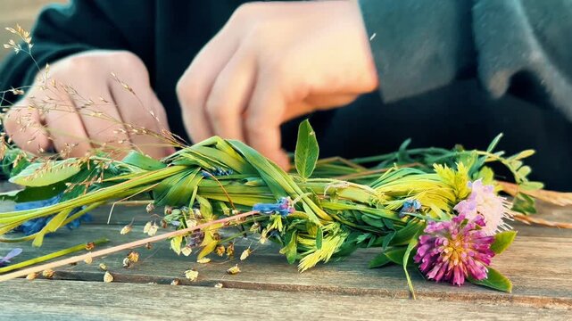 A person weaves a flower crown with clover and grasses. Suitable for eco-friendly product promotions, DIY craft channels, summer festival campaigns, and blog visuals.