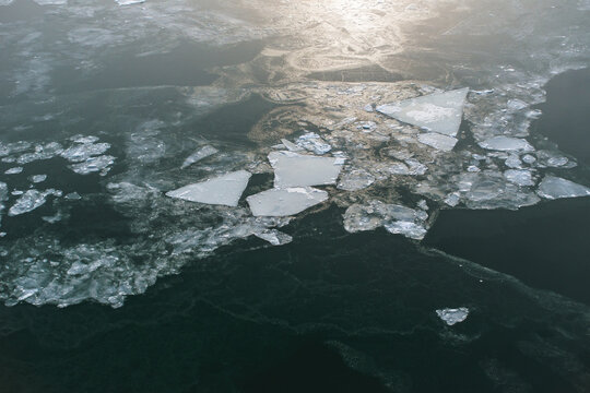 Abstract frozen lake surface with broken ice plates and dark water texture.