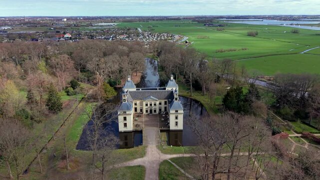 High-angle aerial drone view of a historic symmetrical Dutch castle with a water moat, courtyard, surrounding estate park trees, and green polder fields in the background