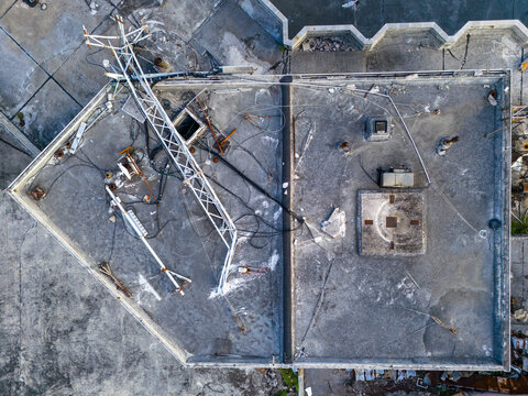 Aerial view of the derelict Tinian Dynasty Hotel rooftop featuring a metal communications tower, scattered cables, and weathered concrete surfaces in San Jose, Tinian, Northern Mariana Islands.