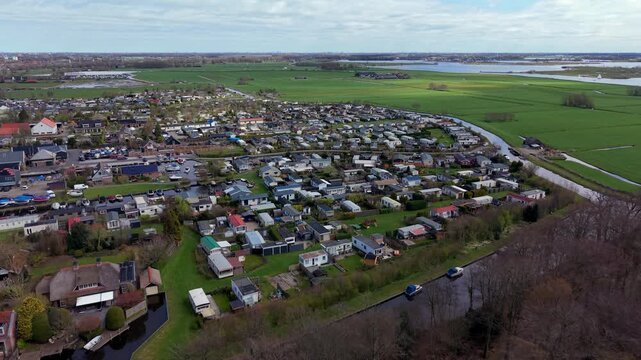 High-angle aerial drone view of a dense Dutch holiday park and trailer campsite situated along a local water canal with expansive green polder fields in the background