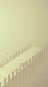 A wooden dock reaches out into still water surrounded by fog. The area looks quiet and empty, with no people present. Morning light gives a soft glow to the scene.