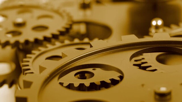 Selective focus close up view of connected mechanical metal gear wheels. Yellow toned machinery system parts, interlocking cogs, and industrial engineering components. Technical mechanical backdrop.