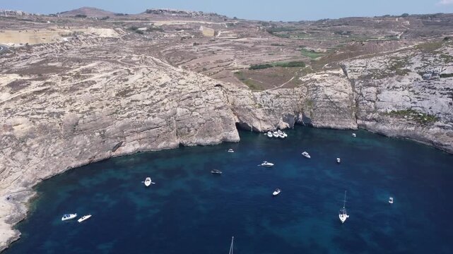 Aerial view of the rugged limestone cliffs of Dwejra Bay with deep blue Mediterranean waters under a clear sky in Gozo region, Malta. High quality 4k footage