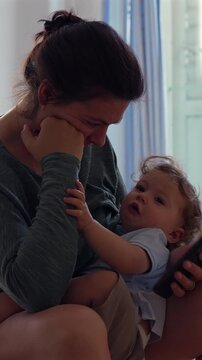Woman breastfeeding toddler while using smartphone at home, highlighting modern parenting, multitasking and everyday family life