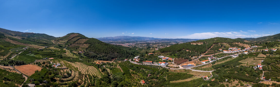 Aerial view of the town of Fundao surrounded by terraced orchards, green hills, and rural roads under a bright blue sky in Fundao, Castelo Branco District, Portugal.