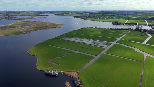 High-angle aerial drone view of traditional Dutch polder landscape with geometric green fields, drainage canals, houseboats, and sailboats navigating a large lake on a bright spring day