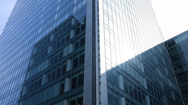 Low-angle view of glass high-rise corner with changing sky reflection and bright specular highlight across reflective curtainwall facades and sharp vertical lines