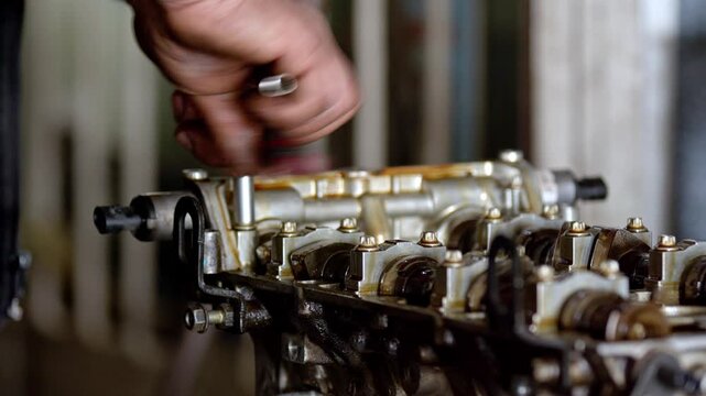 Close up view of mechanic hands using a socket wrench tool to repair or assemble a car cylinder head. Oily metallic automotive engine parts inside a mechanical workshop or garage. Professional vehicle