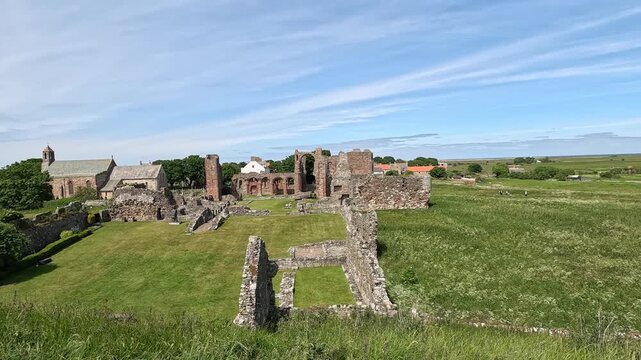 Push-in shot of historic abbey ruins surrounded by lush green grass moving in the wind under bright sunshine, drawing closer to the detail and atmosphere of the ancient site.