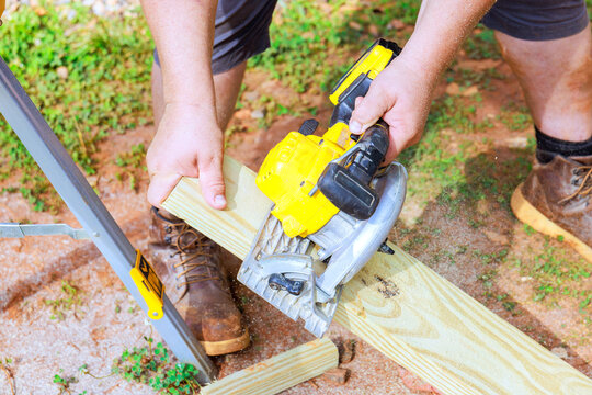Worker works on cutting piece of wood with circular saw in construction area.