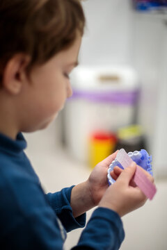 Young boy holding a purple dental jaw model and a pink brushing chart while learning proper teeth cleaning technique at the pediatric dental clinic this afternoon