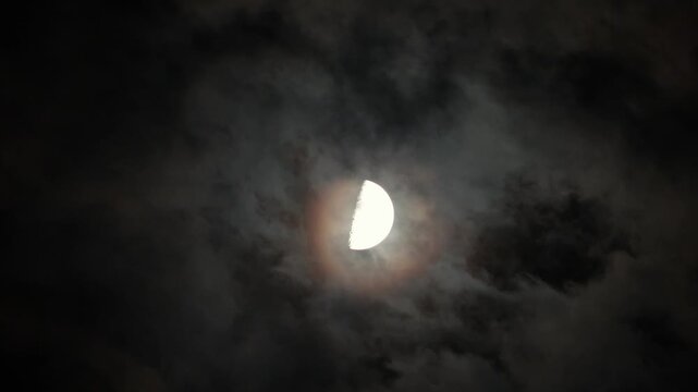 A cloudy night sky with flying clouds and the waxing moon. Moonlight illuminates the clouds in the dark sky