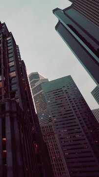 Tall buildings stand close together with glass windows reflecting light. This scene shows the city skyline during late afternoon. The sky appears cloudy above.