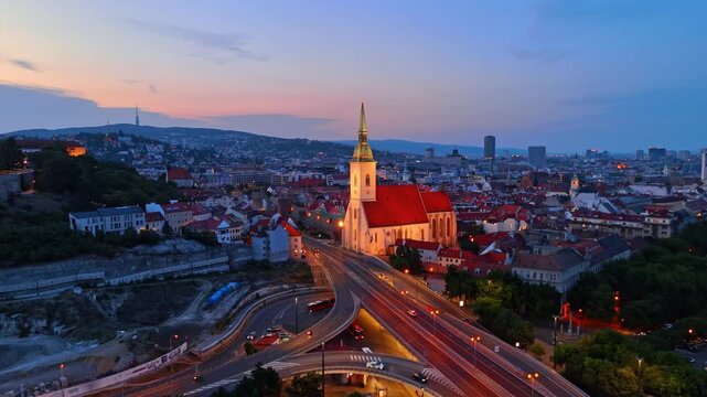 St Martin Cathedral with traffic in Bratislava Slovakia. Evening cityscape showing illuminated church spire and moving car lights on highway overpass.