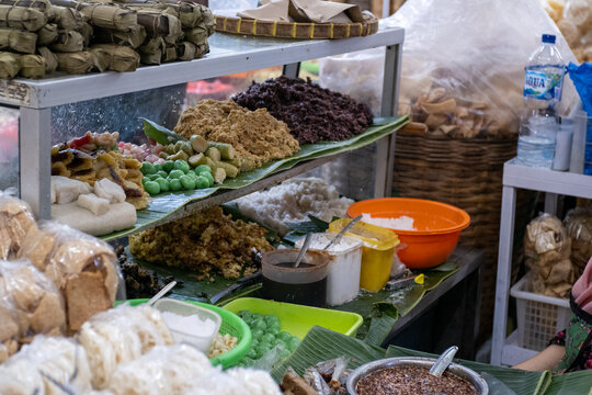 An assortment of traditional Javanese sweet snacks (lenjongan), including cenil, klepon, gethuk, and grontol, displayed on banana leaves inside a glass display cabinet at Pasar Gede, Solo.