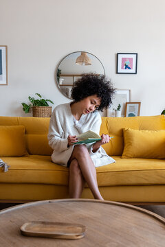 Woman relaxing on yellow sofa reading book at home