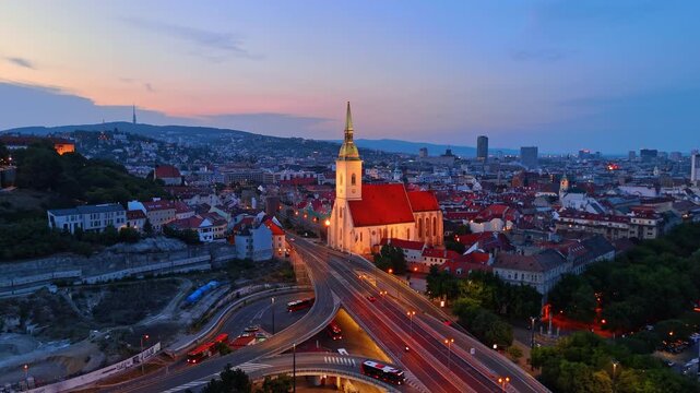 St Martin Cathedral and highway at twilight in Bratislava Slovakia. Illuminated church tower near busy road intersection with car light trails at dusk.