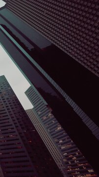 Tall buildings reach towards the sky in a city as lights begin to glow in windows. The scene captures the urban landscape as daylight fades. It showcases architecture and city life.