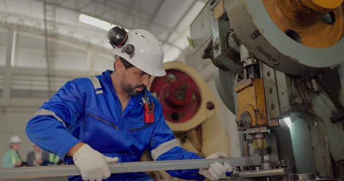 Factory worker operating power press machine to stamp metal bar in manufacturing plant
