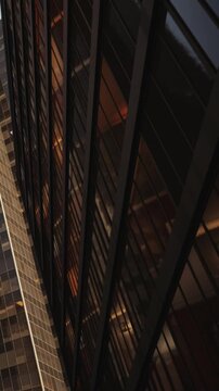 Reflections of light are seen on the glass facade of a tall building in an urban area. The scene shows the interplay of light and structure in the city during the evening.