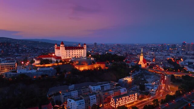 Bratislava Castle and St Martin Cathedral at night Slovakia. Panoramic cityscape showing illuminated fortress and church towers with urban streets at twilight.