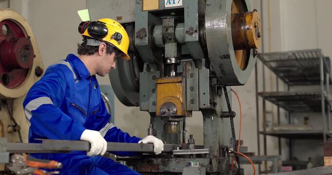 Factory worker operating power press machine to stamp metal bar in manufacturing plant