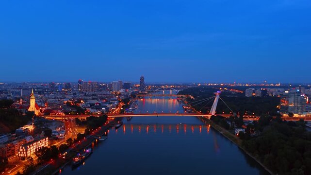 Danube river with illuminated SNP bridge at night, Bratislava. Distant drone shot of glowing transport infrastructure over dark water.