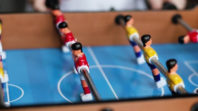 4K Slow motion video of a table football foosball game field. Close up macro shot of red and yellow miniature plastic players spinning on metal rods during a match with a classic soccer ball pattern.