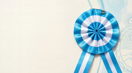 Obraz premium Argentine cockade ribbon on light background. Blue and white escarapela with copy space. Argentina independence day concept