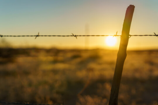 Barbed wire fence and golden morning sunlight background in West Texas.