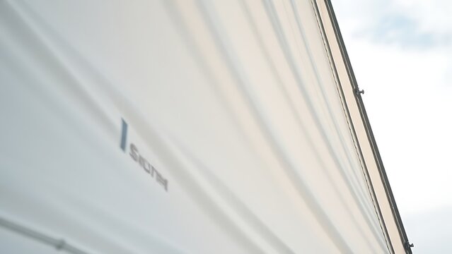 Close-up of sailboat mainsail, heavy canvas billowing taut in wind, visible stitching against soft sky.