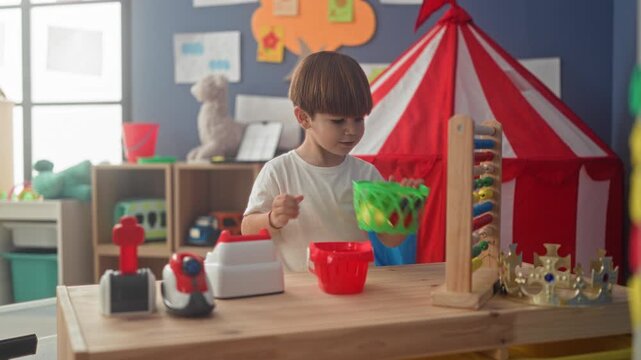 Boy playing with toy cash register and basket, hands on toy on a wooden table, building; curiosity focus.