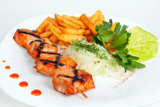 Grilled meat shashlik kebab skewer with golden french fries and fresh green salad on a white plate. Barbecue lunch, hot pork dish,