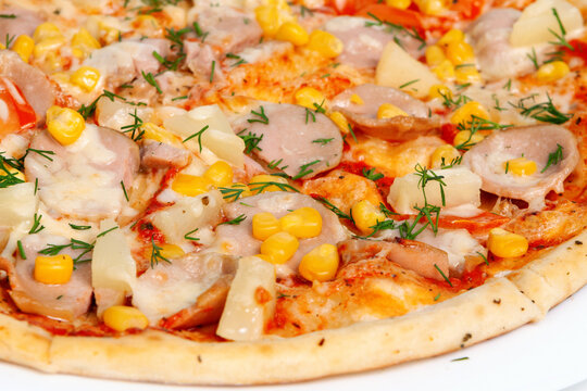 A closeups shot of baked pizza toppings with sliced sausages corn pineapple pieces and fresh herbs.savory dinner dish meal. Dining