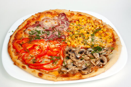Whole baked four seasons pizza with mushrooms ham sweet corn and red bell pepper toppings on a white plate. Italian fast food, delicious cheesy dish, savory dinner meal pastry. Dining.
