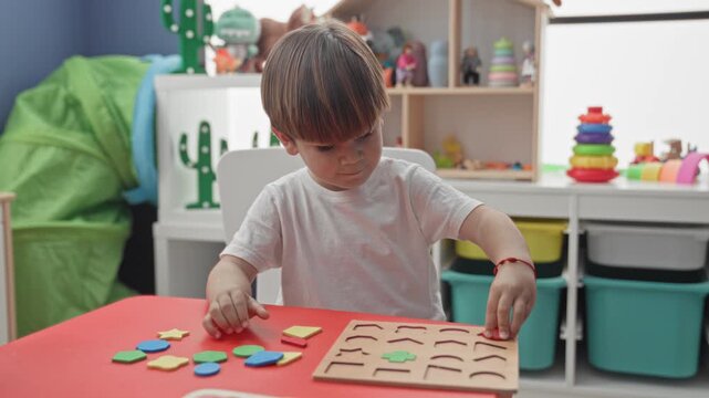 Boy holds a red puzzle piece and sorts wooden shape pieces on a red table in a playroom building; concentration learning play.