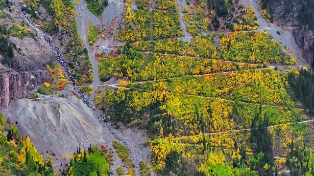 Aerial view of switchbacks on hiking trail to Bridal Veil Falls in mountain ski town of Telluride, Colorado surrounded by fall foliage trees landscape during autumn season - 4K Drone