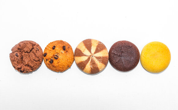 Assorted chocolate cookies and pineapple jam filled cookies isolated on white background. Various types of cookies. Many brown and golden round cookies biscuits arranged in a row