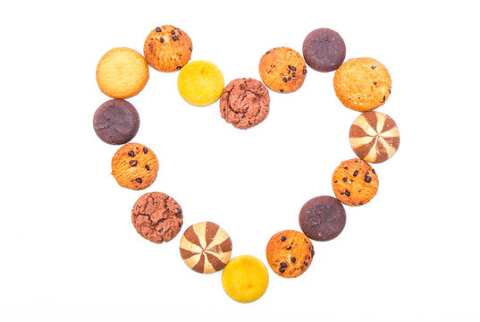 Assorted cookies and biscuits arranged in love shape isolated on white background. Collection of sweet baked snacks including chocolate cookies, butter biscuits, crackers and sandwich cookies.
