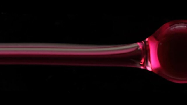 Abstract closeup of a highfrequency darsonvalization glass electrode glowing with a vibrant pink light against a dark background showcasing the intricate details of the medical device