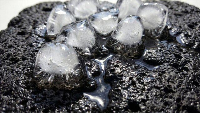 Extreme macro of transparent melting ice cubes on black volcanic stone water streams